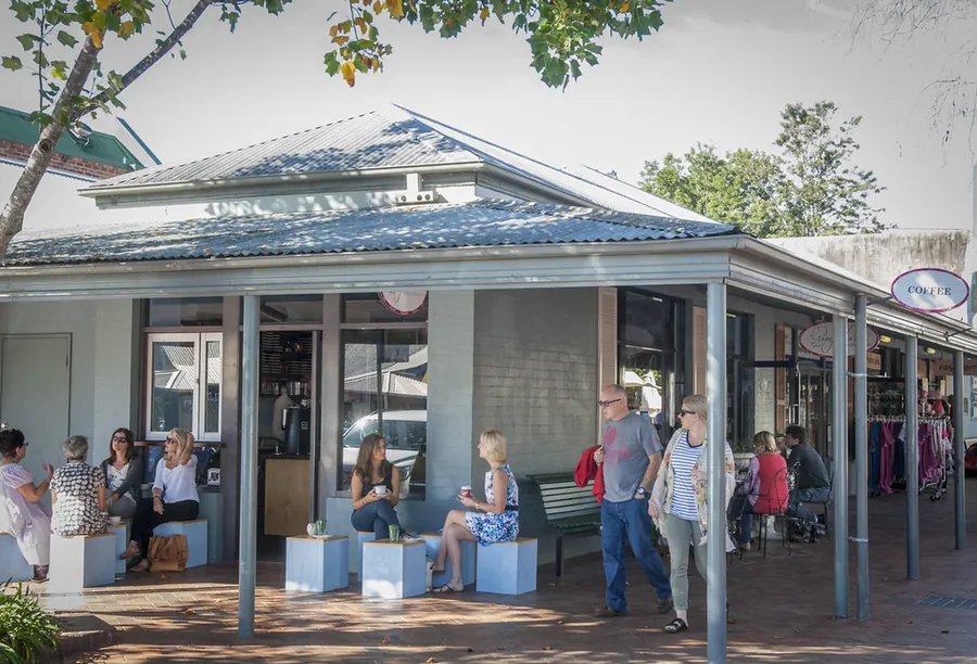 Shoppers sitting on benches under the awning of a corner store on a village street