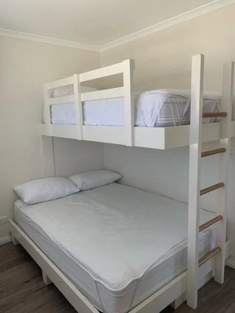 A white timber bunk bed made up in a cabin bedroom, a single bunk above a double bed