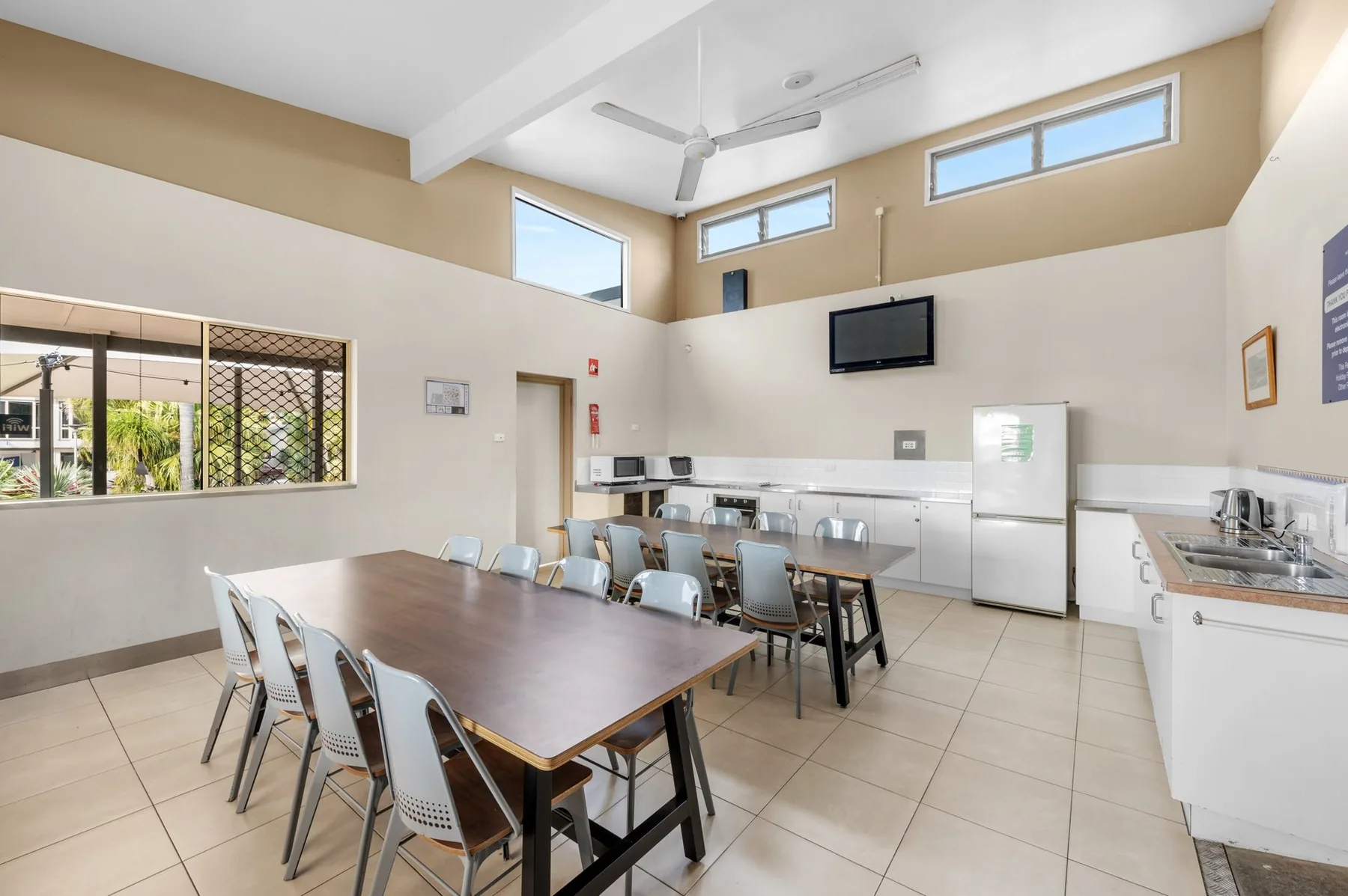 Camp kitchen with a long dining table, cooking benches and a wall-mounted TV