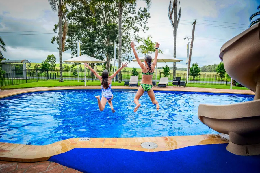 Two children mid-jump into the pool, with shade umbrellas and sun loungers behind