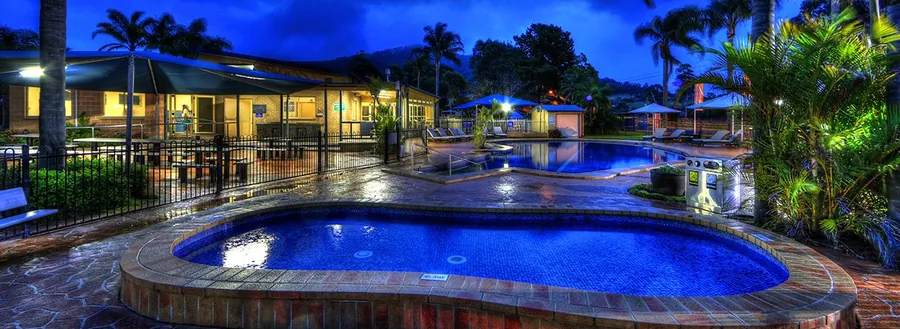 The pool lit from below at dusk, the buildings behind it reflected in the water