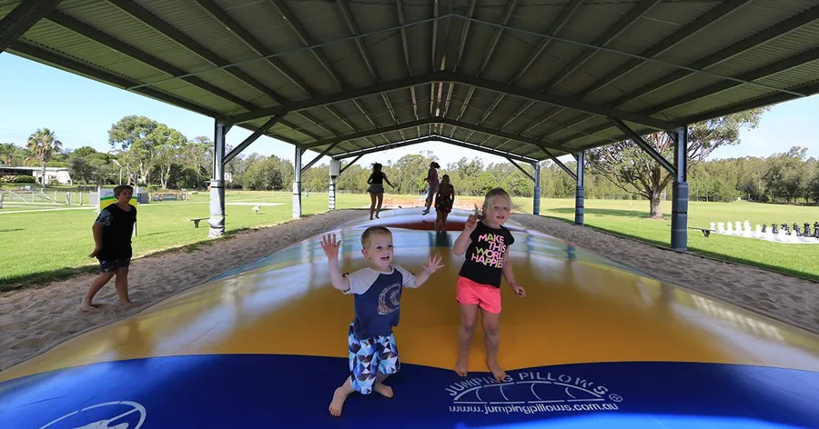 Two small children bouncing on the undercover jumping pillow, open lawn beyond