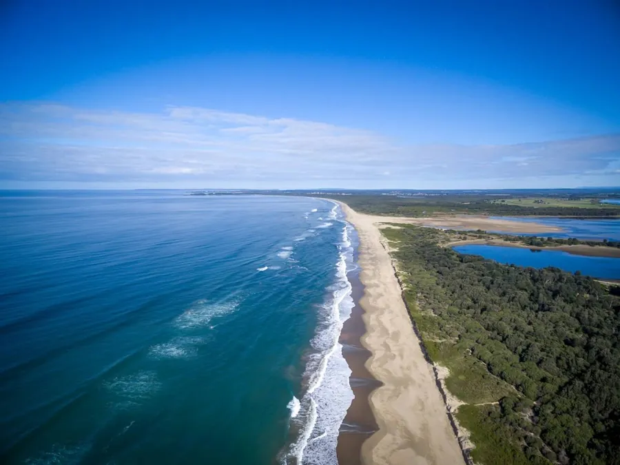 Aerial view along a long surf beach with a lagoon behind the dunes