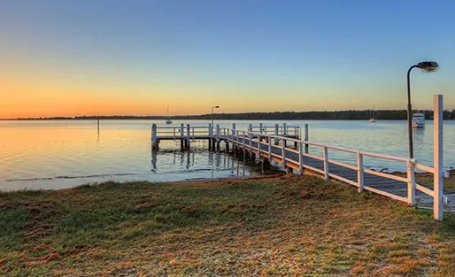 A timber jetty reaching out over calm water at sunset