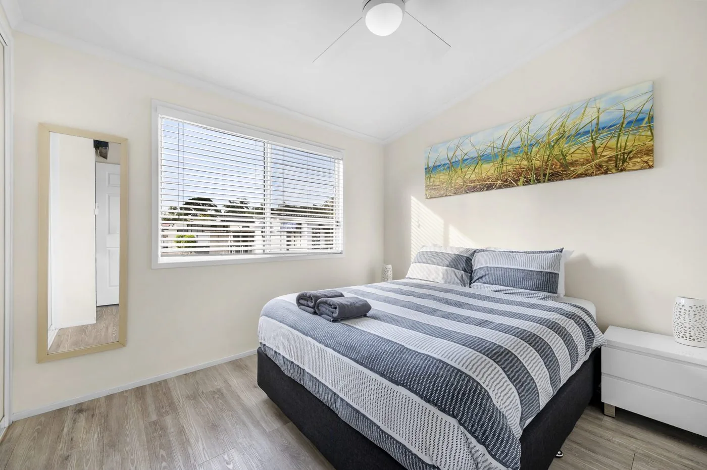 Bedroom with a queen bed, a mirror on the wall and a coastal print