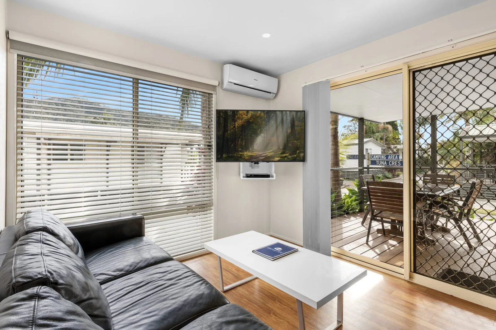 Living area with a corner sofa, wall-mounted TV and doors through to the veranda