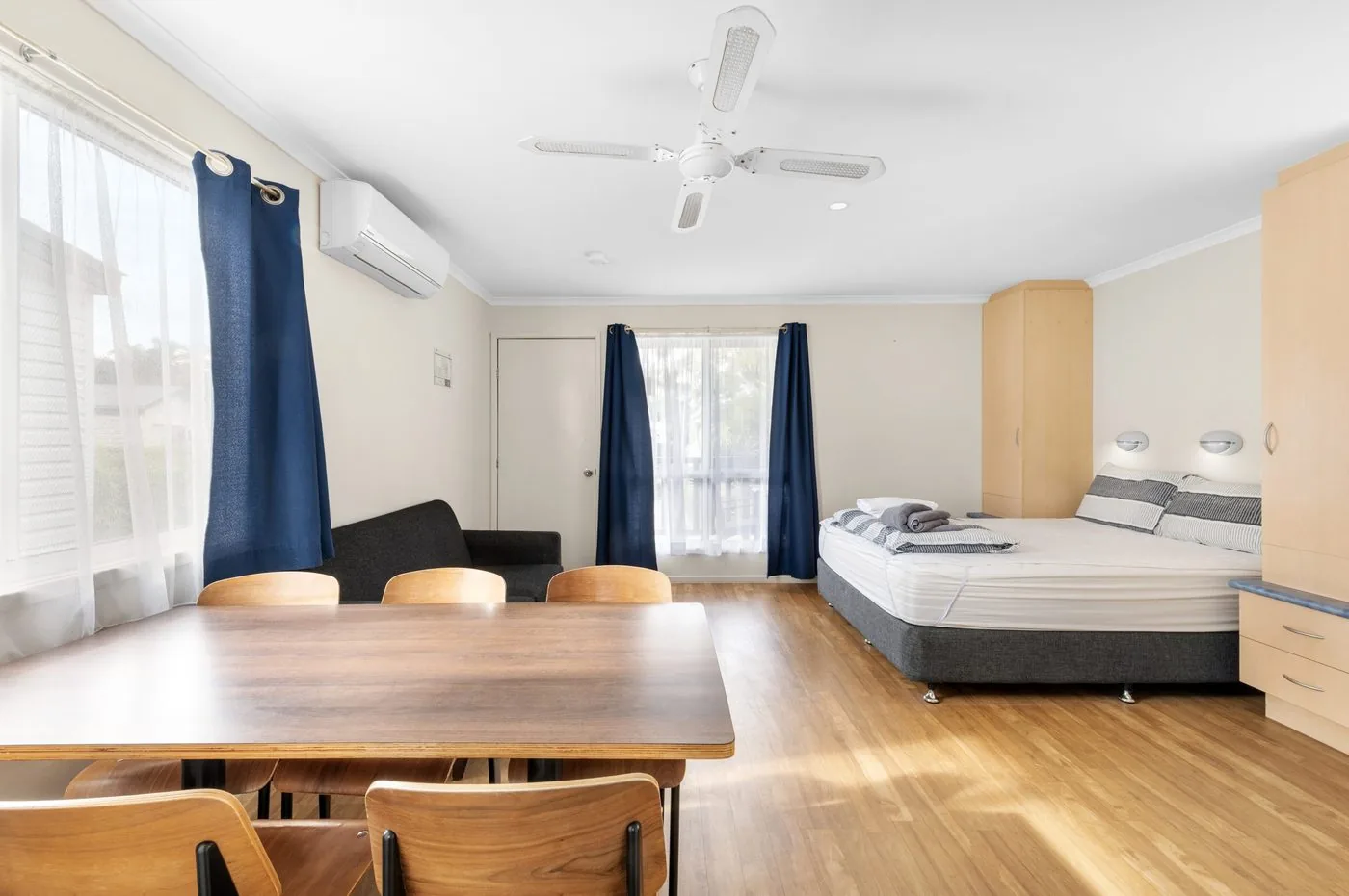 Dining table and chairs with the queen bed and blue curtains behind