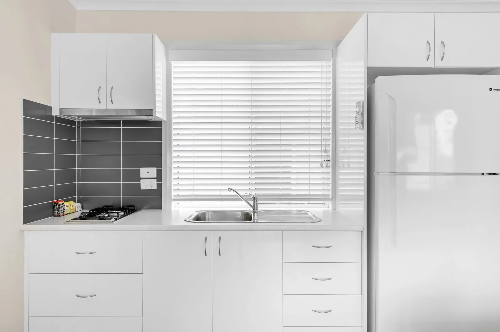 Kitchen bench with a cooktop, sink and a full-height fridge