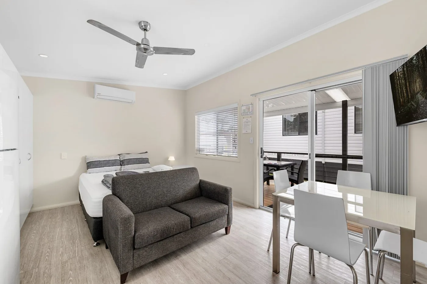 Lounge with a two-seater sofa, dining table and a wall-mounted TV