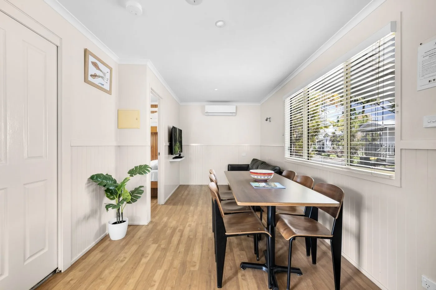 Dining table and chairs below the air-conditioner, with a potted plant in the corner